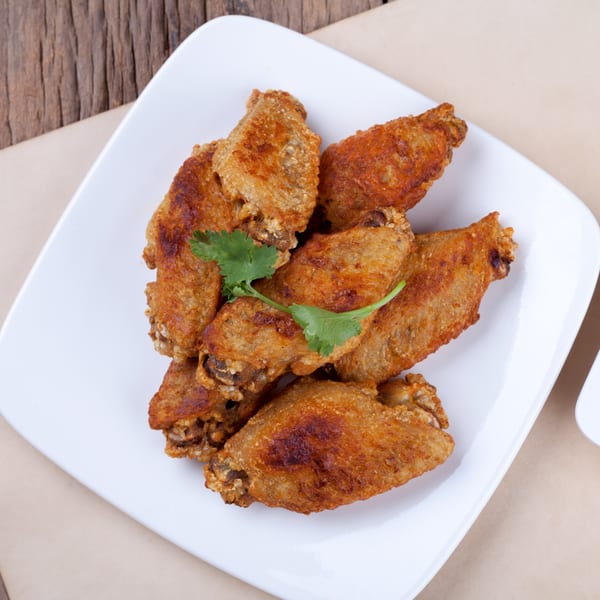 Crispy fried chicken wings garnished with a sprig of cilantro on a white plate at Grace Deli.