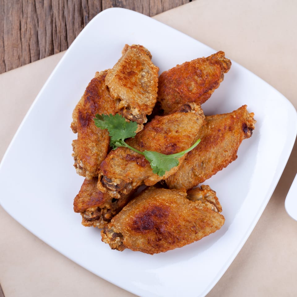 Crispy fried chicken wings garnished with a sprig of cilantro on a white plate at Grace Deli.