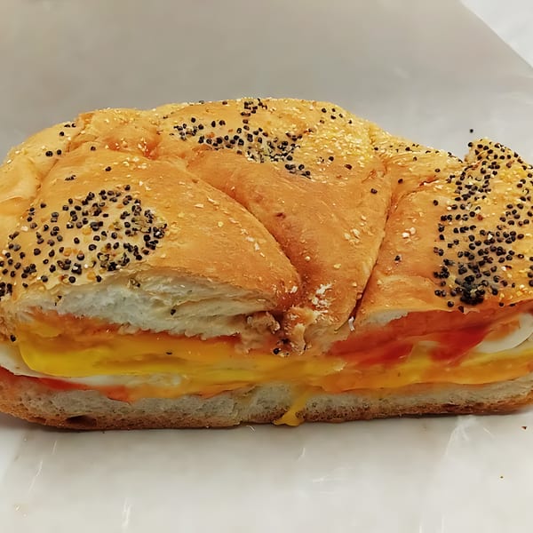 A Grace Deli breakfast sandwich with egg, cheese, and sauce on a poppy seed roll.