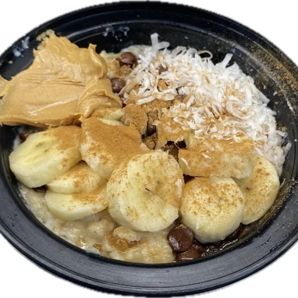 Oatmeal topped with sliced bananas, peanut butter, shredded coconut, chocolate chips, and cinnamon.