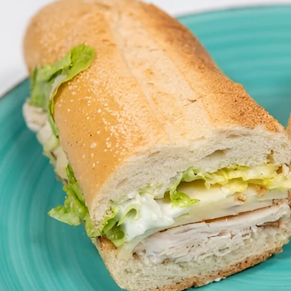 A Grace Deli turkey and cheese sub sandwich with lettuce on a turquoise plate.