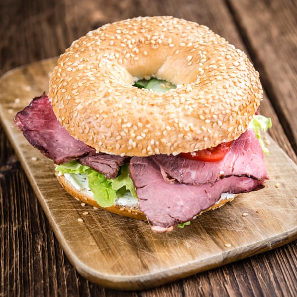 Grace Deli's sesame bagel with roast beef, lettuce, tomato, and cream cheese on a wooden board.
