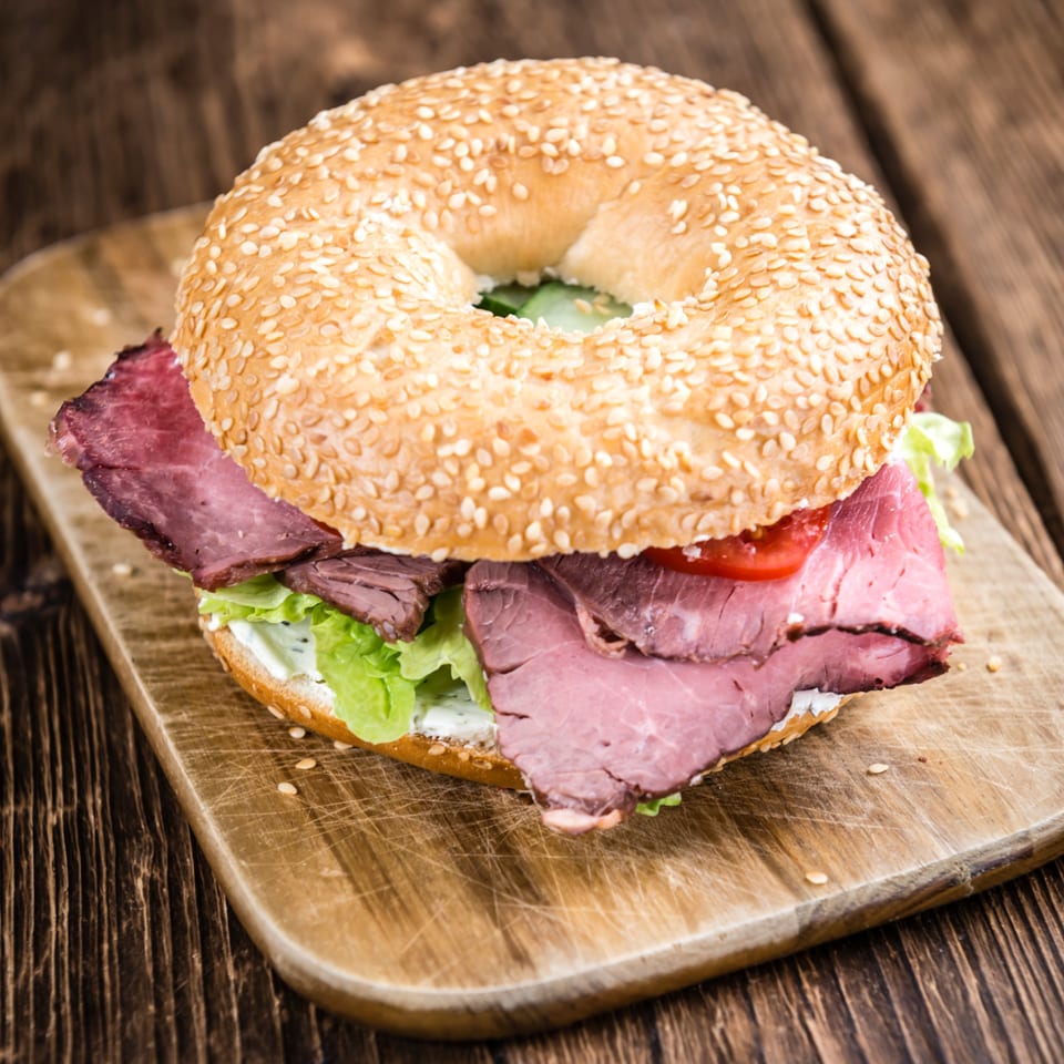 Grace Deli's sesame bagel with roast beef, lettuce, tomato, and cream cheese on a wooden board.