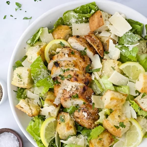 Grace Deli's Caesar salad with grilled chicken, croutons, parmesan, and lemon slices in a white bowl.